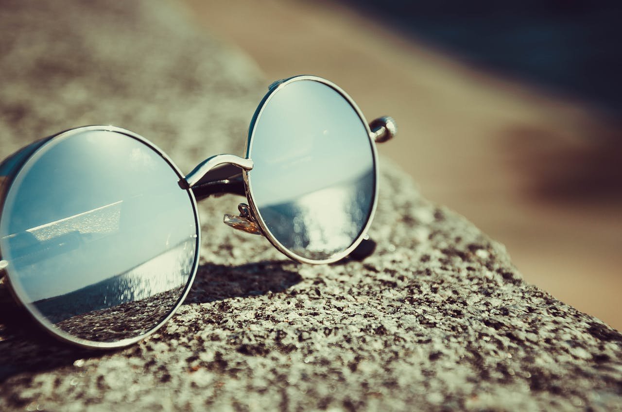 our-services-2 Round sunglasses resting on a sandy beach reflecting the ocean view.